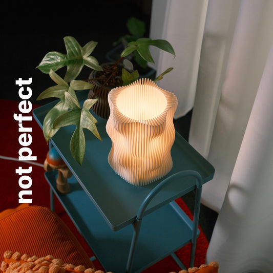 Bubble Lamp in Natural, Not Perfect, glowing on a teal side table beside a plant